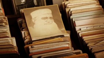 صورة قديمة تُظهر رجل مسن ذو لحية بيضاء، يبدو مبتسمًا، محاطًا بمجموعة من الصور الفوتوغرافية القديمة في ملف. تُظهر الصورة تاريخًا وثقافة غنية من الماضي.