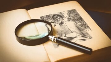 عدسة مكبرة موضوعة على كتاب مفتوح، تظهر صورة لرجل مسن. الكتاب ذو صفحات صفراء، والمشهد يعكس أجواء من البحث والاستكشاف.