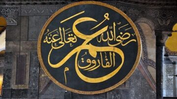 لوحة خطية باللون الذهبي على خلفية داكنة في مكان داخلي.