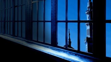 منظر خارجي من نافذة تظهر أبراج مسجد مضاء بلون أزرق داكن، مع تفاصيل معمارية مميزة، في أجواء هادئة.