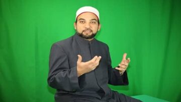 رجل wearing traditional clothing with a white cap يتحدث بإيماءات اليد أمام خلفية خضراء.