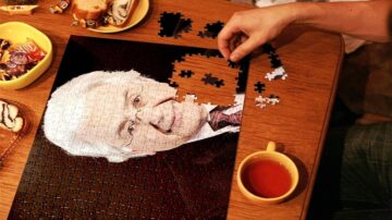 صورة لشخص يعمل على تجميع قطعة ألغاز تظهر وجه شخص مسن. اليد تضع قطعة من الألغاز على الطاولة. بجانب الألغاز توجد أطباق صغيرة تحتوي على حلويات وفنجان شاي.