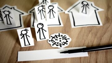 رسومات بسيطة لأشخاص على ورق، موضوعة بجانب بيوت ورقية، مع رسم توضيحي لفيروس في المنتصف وقلم أسود. تعبر الصورة عن موضوع الصحة العامة أو التباعد الاجتماعي.