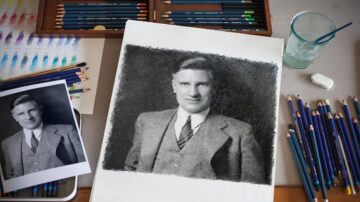 صورة توضح فنانًا يعمل على رسم بورتريه بالألوان الخشبية. يظهر على الطاولة رسم أولي باللونين الأبيض والأسود لشخص يرتدي بدلة، بالإضافة إلى أدوات الرسم مثل أقلام التلوين والزجاجة.