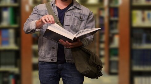 شاب يقف دخا مكتبة عامة ويمسك بكتاب