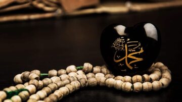 قلب أسود يحمل اسم محمد بتصميم ذهبي، موضوع بجانب سبحة خشبية. تعكس الصورة الجمال الروحي والإيمان.