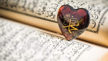 قلب زجاجي أحمر يحمل كلمة "الله" موضوع على صفحات القرآن الكريم، يرمز إلى الإيمان والمحبة الروحية.