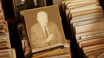 صورة تظهر رجل مسن يتحدث، محاطًا بمجموعة من الصور القديمة في ملف. يبرز التركيز على الشخصية في الصورة الأمامية، بينما تظهر الصور الأخرى في الخلفية بتدرجات ألوان متقاربة، مما يضفي طابعًا تاريخيًا.