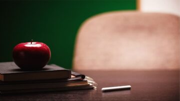 تفاحة حمراء موضوعة على كتب سوداء، بجانب طبعة بيضاء، مع كرسي في الخلفية وجدار أخضر.