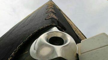 صورة توضح زاوية الكعبة المشرفة، مع التركيز على الحجر الأسود وأجزاء من غلاف الكعبة الأسود المزخرف بالذهب. السماء تظهر في الخلفية، مما يضيف عمقًا للصورة.