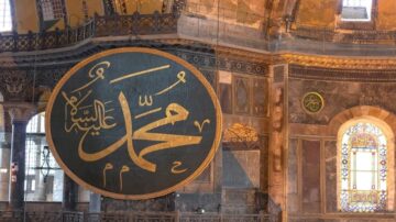 لوحة كبيرة تحمل اسم محمد بالخط العربي، تتواجد في قبة آيا صوفيا، مع تفاصيل معمارية تاريخية تحيط بها.