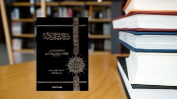 كتاب في مكتبة مع مجموعة من الكتب. الغلاف أسود مزخرف بكتابة عربية. يبرز الكتاب على طاولة خشبية.