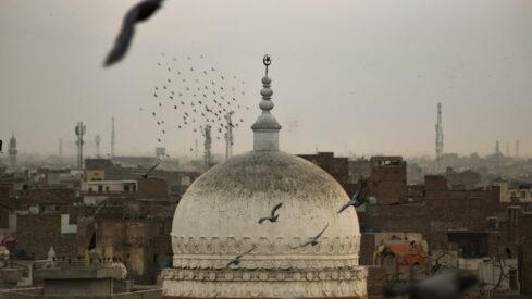 قبة بيضاء كبيرة مع هلال ونجمة، تحيط بها طيور في سماء غائمة فوق المدينة.