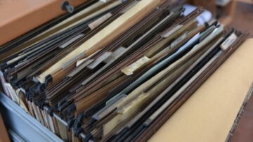 مجموعة من الملفات الورقية مرتبة داخل درج، تحتوي على أوراق ومستندات بألوان مختلفة، تعكس بيئة مكتبية منظمة.