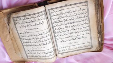 كتاب قديم مفتوح يظهر صفحات تحتوي على نصوص باللغة العربية، مع تصميم كلاسيكي وإطار مزخرف. الكتاب يبدو worn ومرتدي، مما يدل على عمره التاريخي.