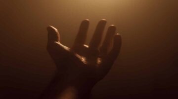 يد مرفوعة نحو الضوء في بيئة ضبابية، مما يخلق إحساسًا بالأمل والتواصل.