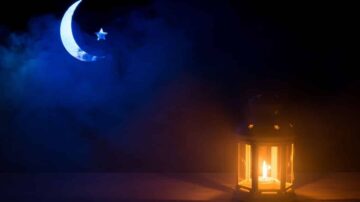 فانوس مضاء بلهب يتلألأ في الظلام بجانب قمر هلال ونجمة في سماء ملبدة بالغيوم.
