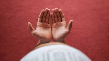 أيدٍ مفتوحة نحو السماء على سطح أحمر، تعبر عن الإيمان أو الدعاء.