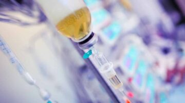 زجاجة سوائل طبية تتدفق منها السوائل عبر أنبوب إلى جهاز طبي في بيئة مستشفى. تظهر خلفية غير واضحة لأجهزة طبية أخرى.