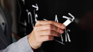 يد تظهر وهي تمسح كتابات رياضية على سبورة سوداء، مع التركيز على الرموز والمعادلات الرياضية.