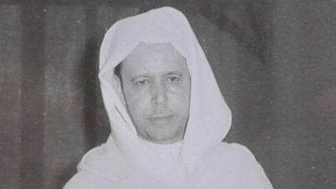 صورة تاريخية لرجل يرتدي جلباب أبيض وعمامة، يظهر بملامح جادة، في خلفية غير واضحة. تعكس الصورة الطابع الثقافي والزي التقليدي.