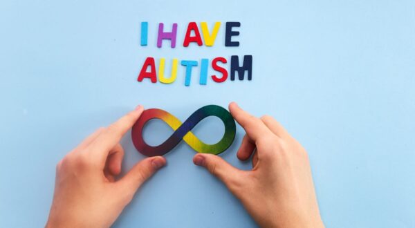 يد تحمل رمز اللانهاية الملون مع نص "لدي توحد" مكتوب بأحرف ملونة على خلفية زرقاء.