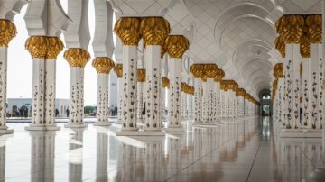 أعمدة مزخرفة بذهب وبياض في مسجد الشيخ زايد، تعكس الضوء على أرضية رخامية لامعة، تعبر عن جمال العمارة الإسلامية.