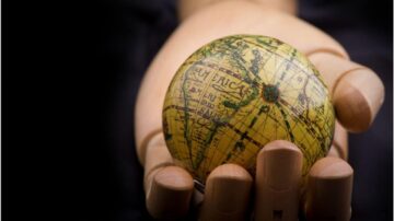 كرة أرضية صغيرة تحملها يد خشبية، تظهر تفاصيل القارات والمحيطات بشكل واضح، مع خلفية داكنة تسلط الضوء على الكوكب.