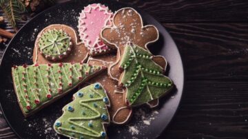 بسكويت الزنجبيل المزخرف بأشكال عيد الميلاد، بما في ذلك شجرة خضراء، رجل زنجبيل، وحلويات ملونة، موضوعة على طبق أسود مع رشات من السكر.