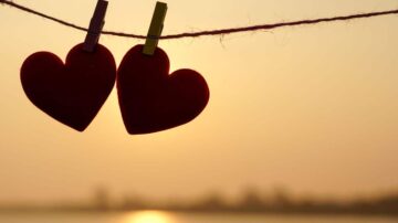 قلوب حمراء معلقة على حبل مع غروب الشمس في الخلفية، تعبير عن الحب والرومانسية.