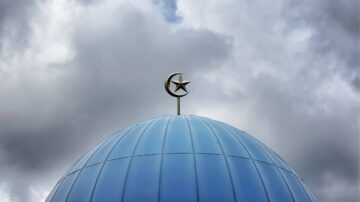 قبة زرقاء مع هلال ونجمة في الأعلى، تحت سماء غائمة. تعكس الصورة العمارة الإسلامية والرموز الثقافية.