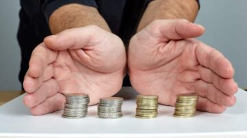 أيدٍ مفتوحة تحمل عملات معدنية فضية وذهبية مرتبة في صفوف، تظهر تباين القيمة بين العملات.