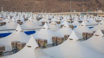 خيام بيضاء متعددة بأشكال مخروطية في منطقة مرتفعة، تظهر في الخلفية جبال جافة، مع وجود وحدات تكييف هواء على بعض الخيام. تعكس الصورة مشهدًا من تنظيم فعاليات أو تجمعات كبيرة.