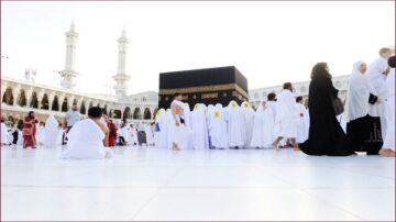 موسم الحج في الكعبة المشرفة، حجاج يرتدون ملابس الإحرام البيضاء، مجموعة من الأشخاص من جنسيات مختلفة حول الكعبة، مشهد يعكس روحانية الحج وأجواء العبادة في مكة.