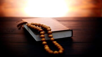 كتاب مفتوح مع مسبحة خشبية موضوعة فوقه، في خلفية ضوء الشمس الساطع. يُبرز المشهد الأجواء الروحية والتأملية.