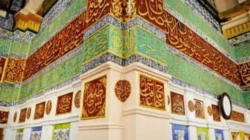 جدار مزخرف بألوان زاهية في موقع تاريخي، يحتوي على نقوش عربية وأشكال هندسية. يظهر في الصورة نصوص إسلامية مكتوبة بخطوط فنية، مع تفاصيل ملونة تعكس التراث الثقافي.