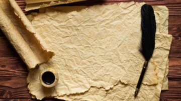 ورقة قديمة ومجعدة مع قلم ريش وحبر، موضوعة على سطح خشبي.