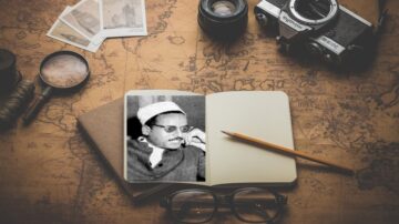 صورة تظهر دفتر ملاحظات مفتوح على خريطة قديمة، مع صورة تذكارية لشخص يرتدي نظارات وقبعة. بجانب الدفتر، توجد كاميرا قديمة وعدد من الصور الفوتوغرافية. تعكس الصورة جوًا من الاستكشاف والذكريات.