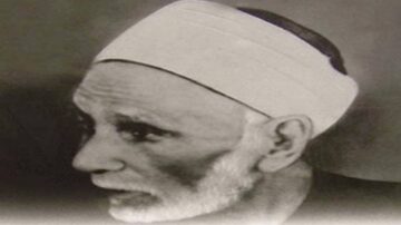 صورة تاريخية لرجل مسن ذو لحية وشعر أبيض، يرتدي غطاء رأس أبيض. تعكس ملامحه الحكمة والخبرة.