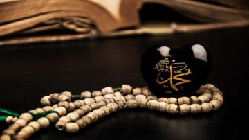 حجر على شكل قلب مكتوب عليه اسم محمد، موضوع على طاولة بجانب مصحف وسبحة خشبية.