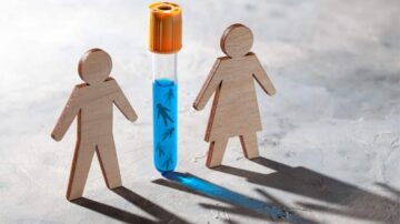 أنبوب اختبار يحتوي على سائل أزرق مع شخصيات خشبية تمثل الجنسين، واحدة ذكورية والأخرى أنثوية، في بيئة رمادية.