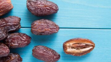 تمر بني اللون على سطح خشبي أزرق، مع قطعة مقطوعة تظهر النواة الداخلية.