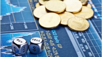 صورة لسطح مكتب مالي يظهر فيه عملات نقدية وقطع نرد مكتوب عليها "شراء" و"بيع". خلفية الصورة تحتوي على مخطط بياني يشير إلى حركة السوق المالية.