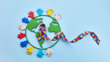 صورة تظهر خريطة للعالم محاطة بأيدٍ ملونة، مع شريط ملون يحمل رموز الألغاز. تعبر الصورة عن دعم التوعية بالتوحد وتعزيز القيم العالمية للتضامن والشمولية.