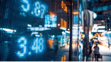 شاشة عرض رقمية تعرض أسعار الأسهم مع أضواء خلفية زرقاء، مشهد حضري في وقت المساء.