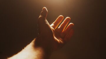 يد ممدودة نحو الضوء في بيئة مظلمة، تعكس الإحساس بالأمل والتواصل.