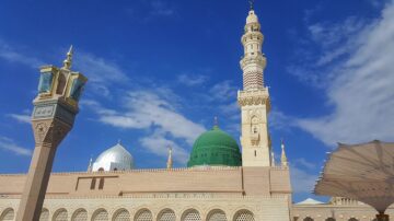 مسجد النبي في المدينة المنورة مع قبة خضراء ومنارة مرتفعة تحت سماء زرقاء.