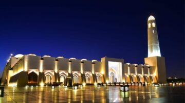 مسجد معمار حديث مضاء في الليل، يعكس جمال التصميم المعماري الإسلامي. يبرز المئذنة العالية في الخلفية مع سماء زرقاء غامقة، مما يضيف لمسة ساحرة للمشهد.