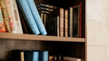 رفوف خشبية تحتوي على مجموعة من الكتب ذات أغلفة ملونة وفاخرة، مع تصميمات تقليدية. الكتب مرتبة بشكل منظم، مما يبرز جمالها وتنوعها.