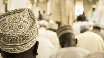 مجموعة من الأشخاص في وضع الصلاة في مسجد، تظهر رؤوسهم مغطاة بأغطية تقليدية. الخلفية ضبابية، مما يبرز التركيز على الأفراد أثناء أداء شعائرهم الدينية.